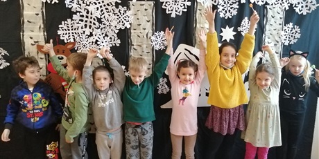 Powiększ grafikę: Klasa pierwsza. Uczniowie z wyciągniętymi rękoma do góry na tle zimowej dekoracji.